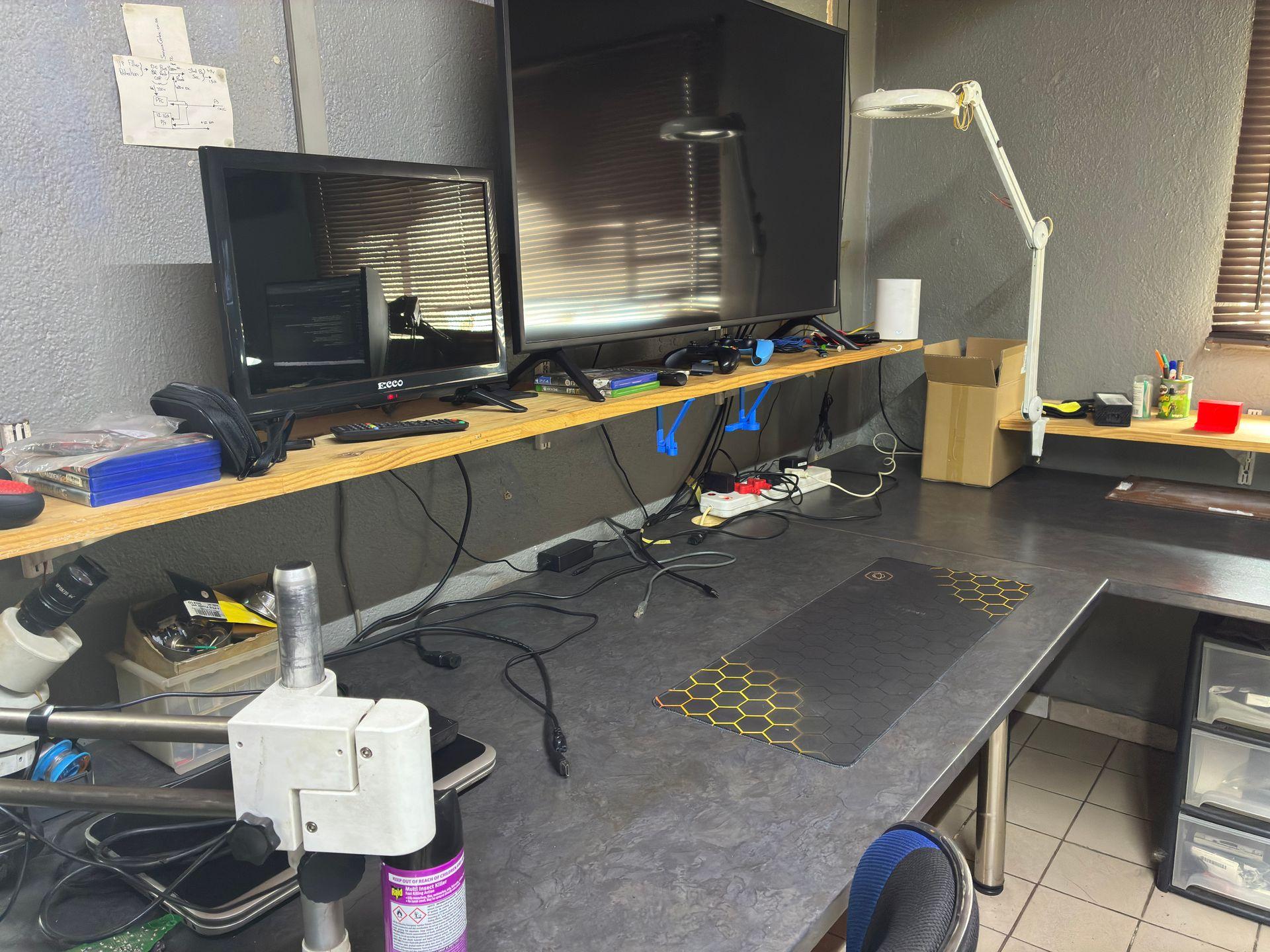 Console testing and diagnostics station with multiple monitors and magnifying lamp at Console Service Centre Boksburg