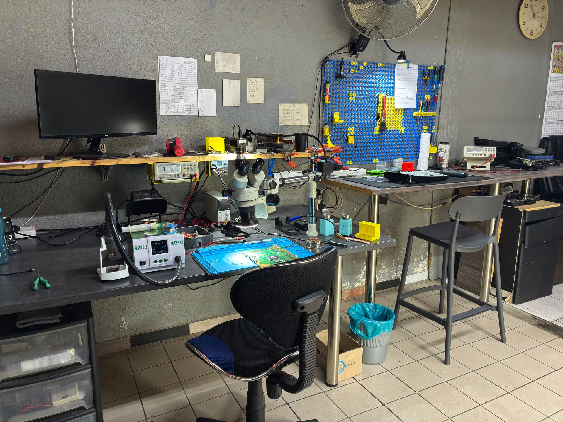 Repair workstation with microscope and pegboard tool wall used for PS5 disc drive repairs